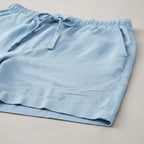 Folded light blue shorts on a flat surface showing the hem, drawstring tie and relaxed leg shape