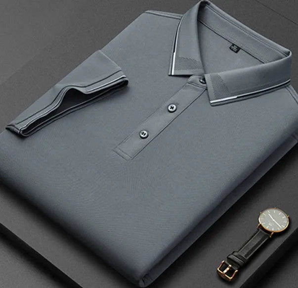 Folded grey polo shirt with white piped collar and cuffs, placed next to a wristwatch