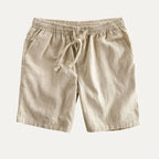 Beige linen shorts laid flat, showing elastic drawstring waist, side pockets and soft pleated texture