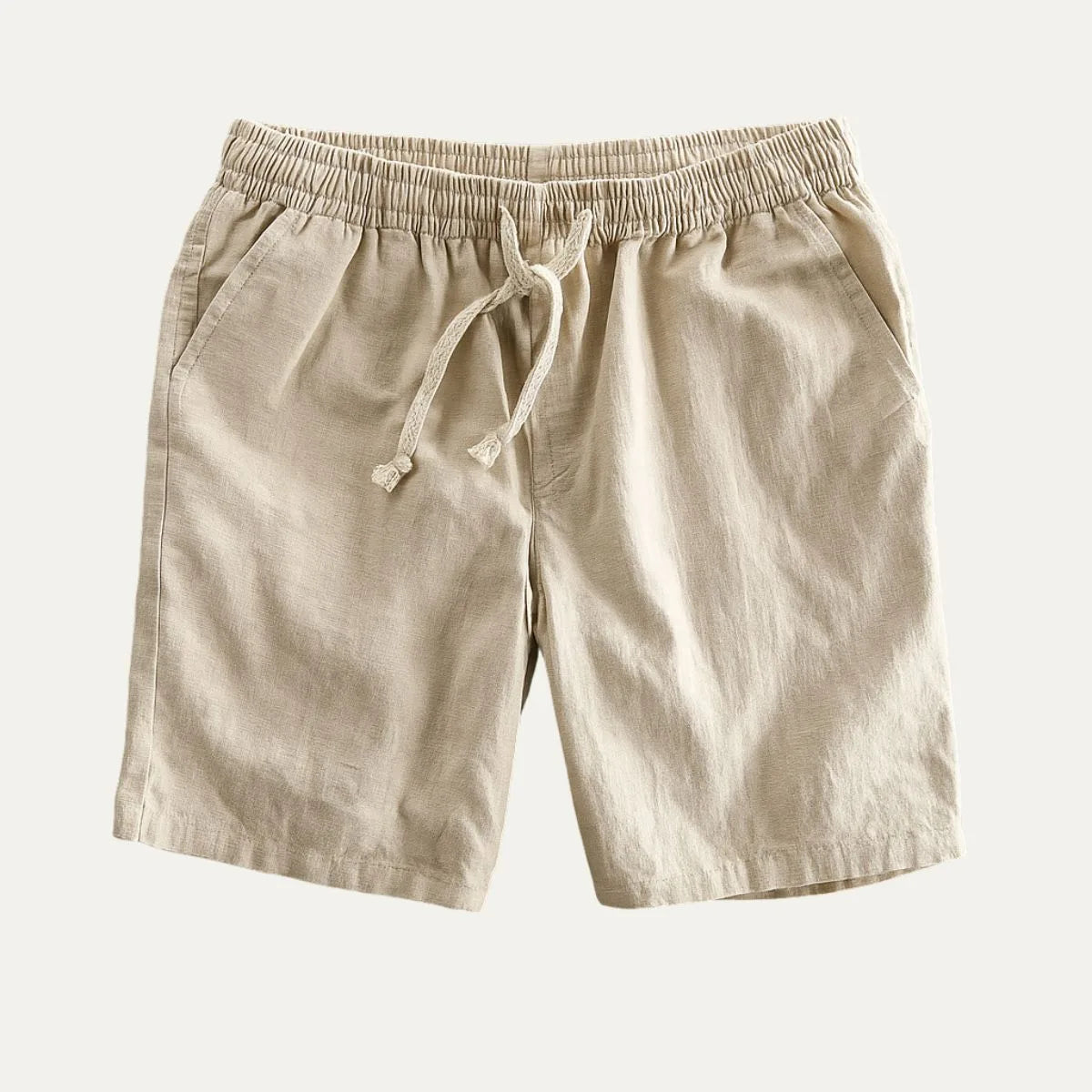 Beige linen shorts laid flat, showing elastic drawstring waist, side pockets and soft pleated texture