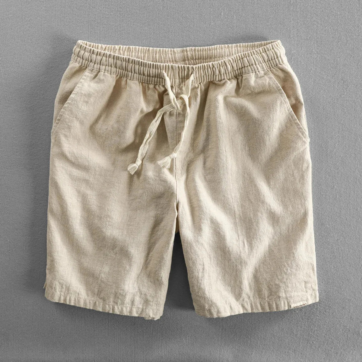 Beige linen shorts flat lay on grey background, showing fabric weave and side pocket opening
