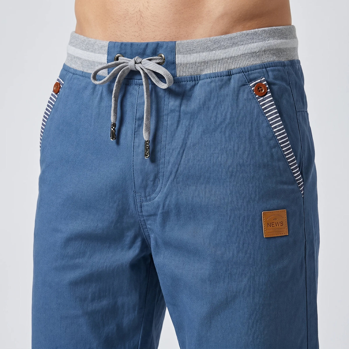 Close-up of steel blue shorts waistband showing grey ribbed band, drawstring toggles and leather logo patch