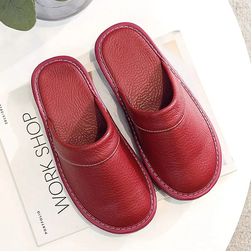 Black leather slipper pair viewed from above resting on a tiled floor, showing the slip-on open-back cut.