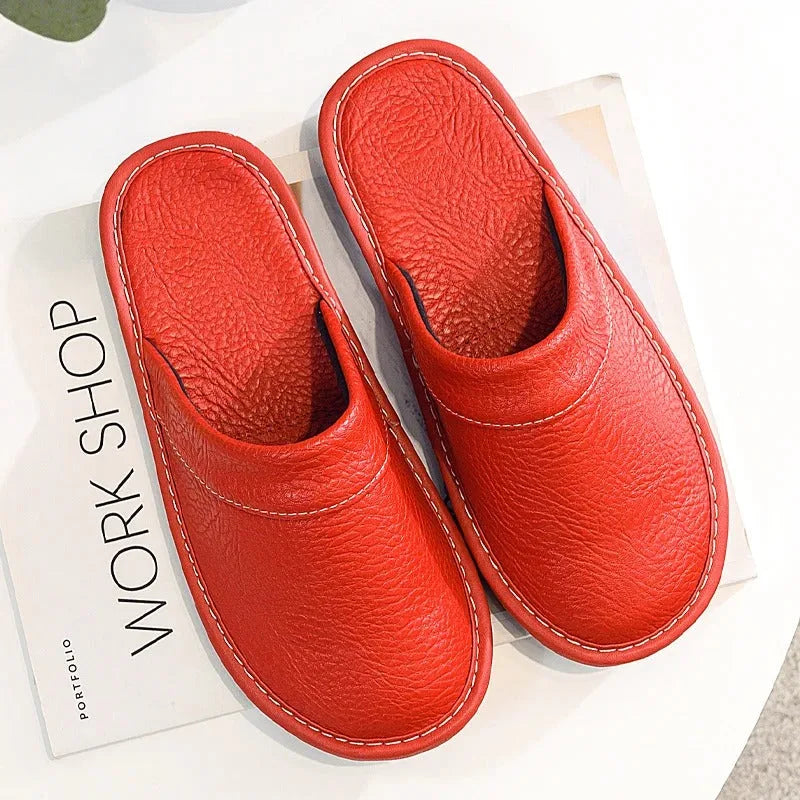 Navy leather slipper shown on a bare foot with grey trousers, highlighting the smooth leather grain and stitch trim.