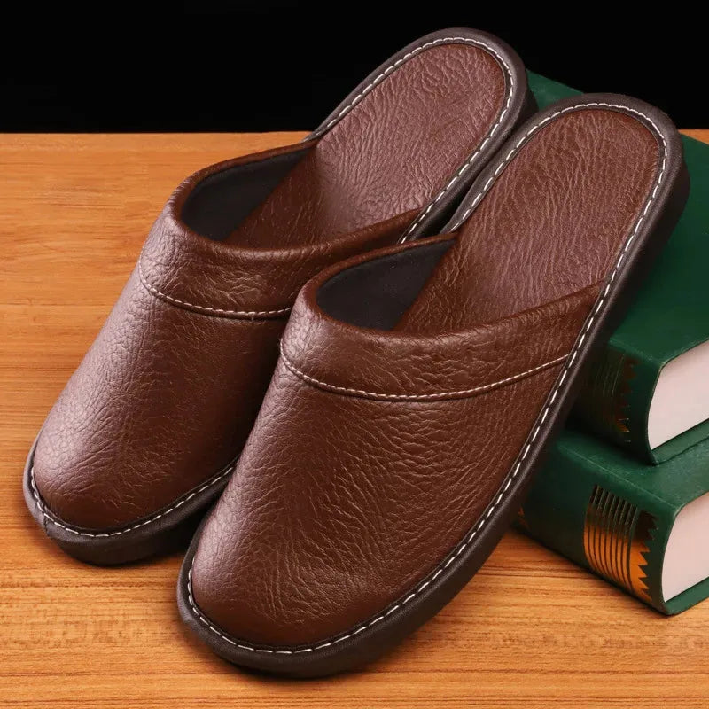 Pair of brown leather slide slippers with contrast stitching resting against green books on a timber tabletop
