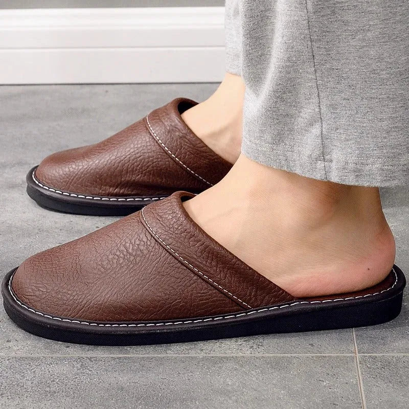 Side profile of brown leather slippers worn with grey trousers, highlighting the low-cut vamp and black outsole.