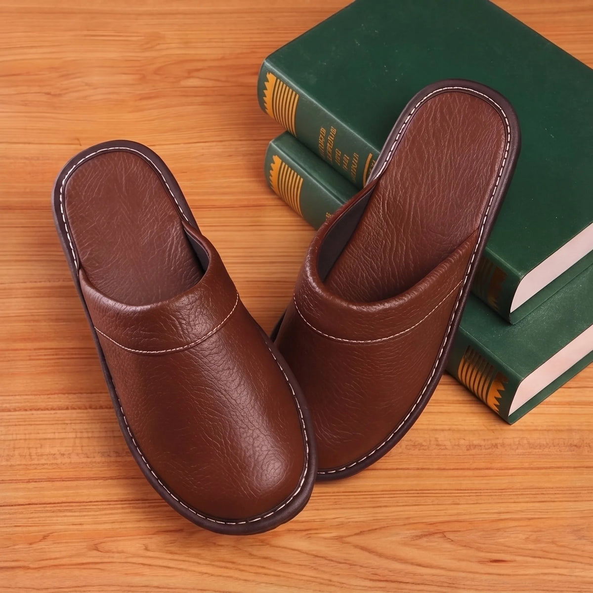 Overhead view of brown leather slippers showing padded insole and curved stitched trim beside stacked books