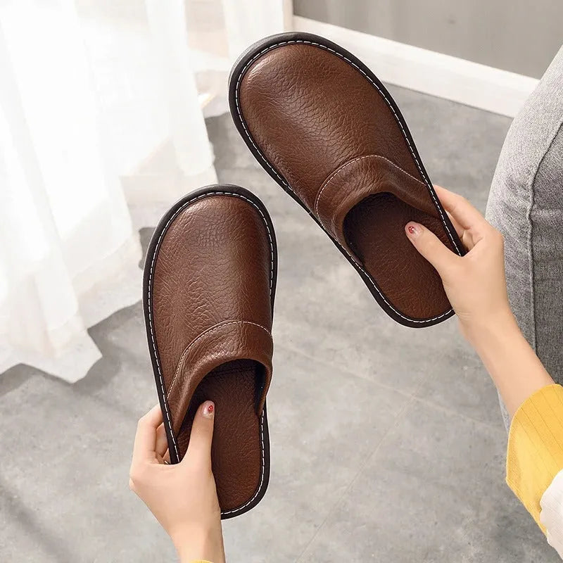Pair of brown leather slippers held by hand, showing the soft cushioned footbed and rolled heel collar.