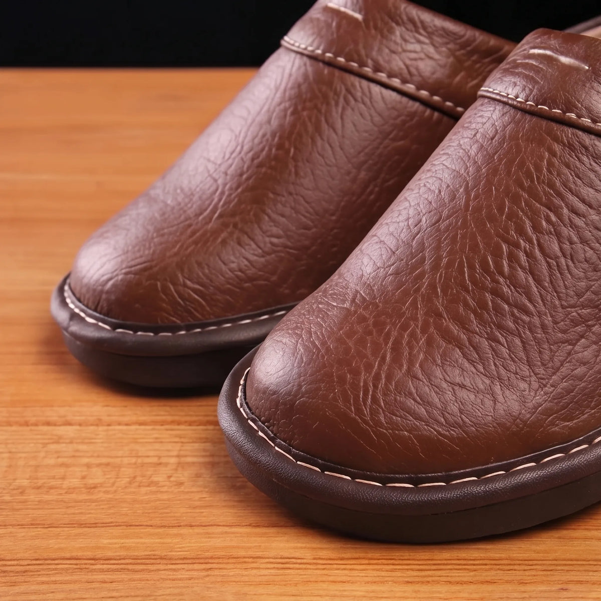 Close-up of the textured brown leather upper with visible grain and cream topstitching detail