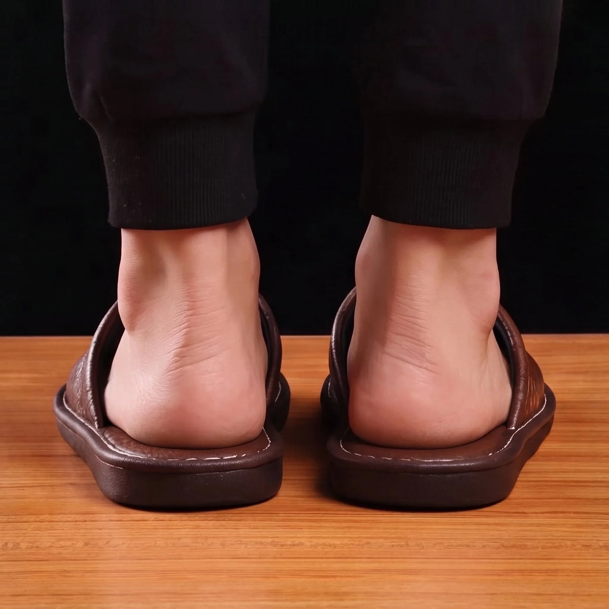 Rear view of a person's feet slipped into the brown leather mule slippers on a wooden floor