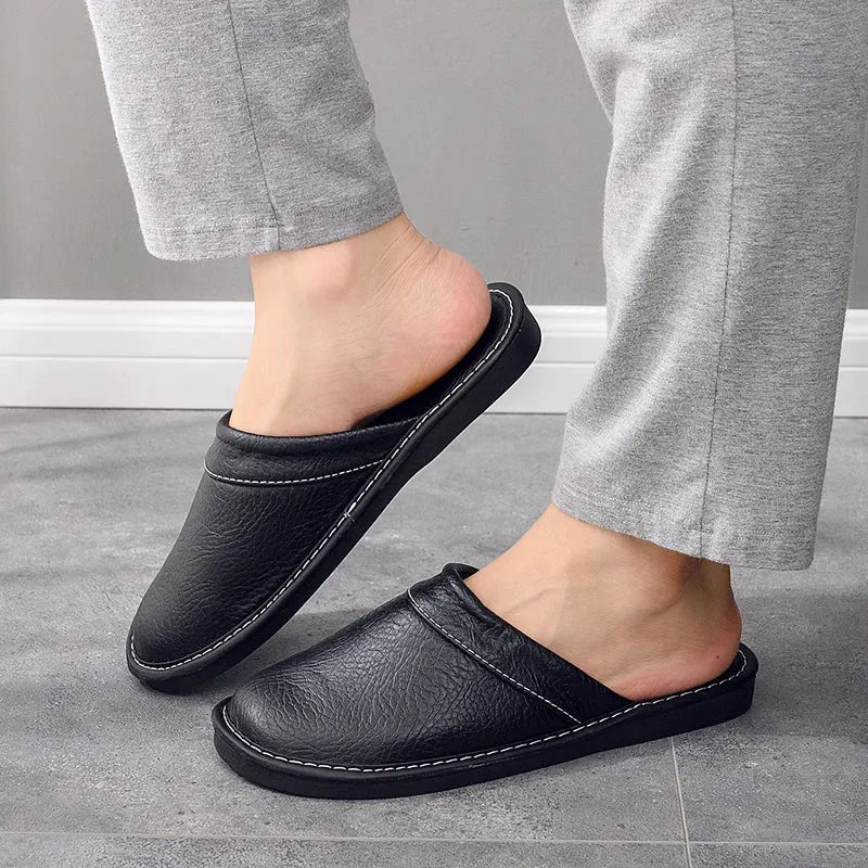 Side profile of a black leather mule slipper worn with grey trousers, showing low-cut backless heel