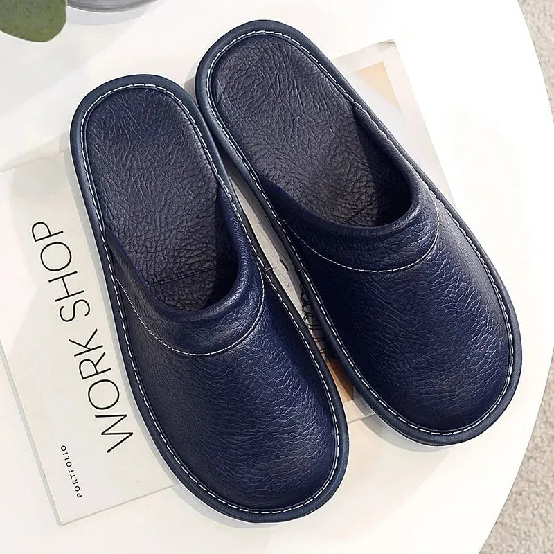 Overhead flat-lay of a pair of navy blue leather slippers on a white surface, showing the full length and curved shape.