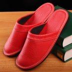 Overhead view of glossy red leather slide slippers with stitched edging held above a wooden floor