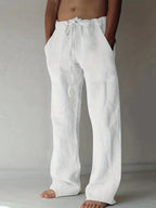 Front view of white linen drawstring pants with relaxed wide legs and side pockets, worn barefoot