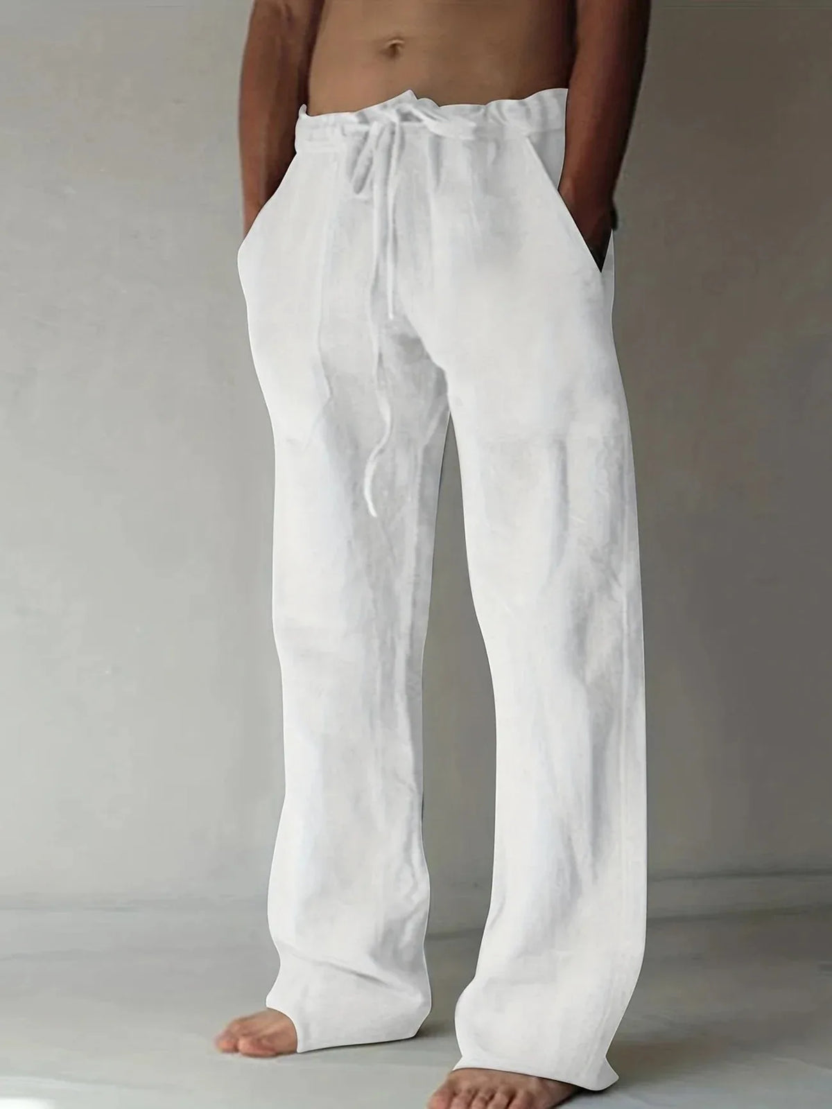 Front view of white linen drawstring pants with relaxed wide legs and side pockets, worn barefoot