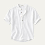 Flat lay of a white short-sleeve linen shirt with a band collar and wooden-look buttons, folded cuffs