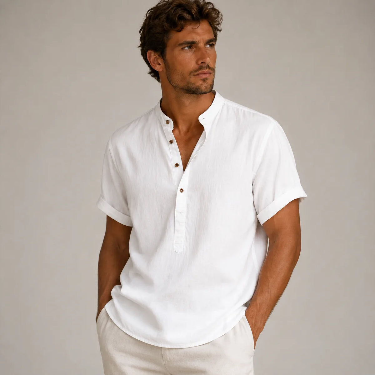 Man wearing a white band-collar linen shirt with rolled sleeves, unbuttoned at the top, paired with beige pants