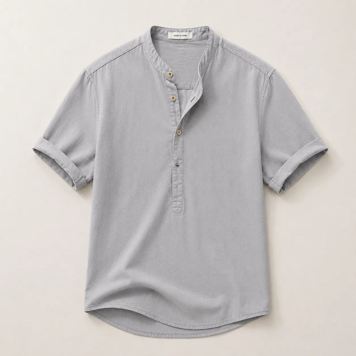 Flat lay of a grey short-sleeve linen shirt showing the collarless band neckline and folded sleeve cuffs