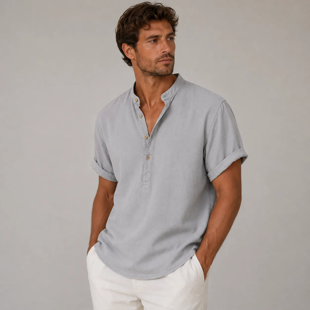 Man modelling a grey band-collar linen shirt with sleeves rolled, worn open-necked over cream trousers