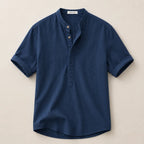 Flat lay of a navy blue linen shirt with band collar, button placket and rolled short sleeves