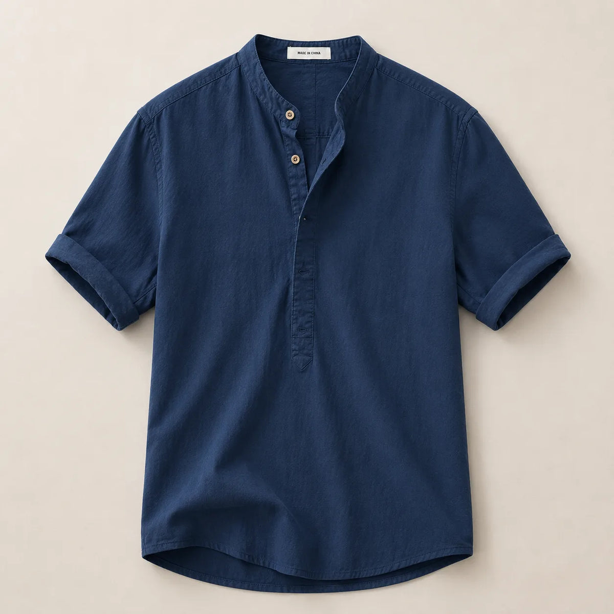 Flat lay of a navy blue linen shirt with band collar, button placket and rolled short sleeves