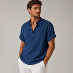 Man wearing a navy blue band-collar linen shirt with rolled cuffs, styled with white pants