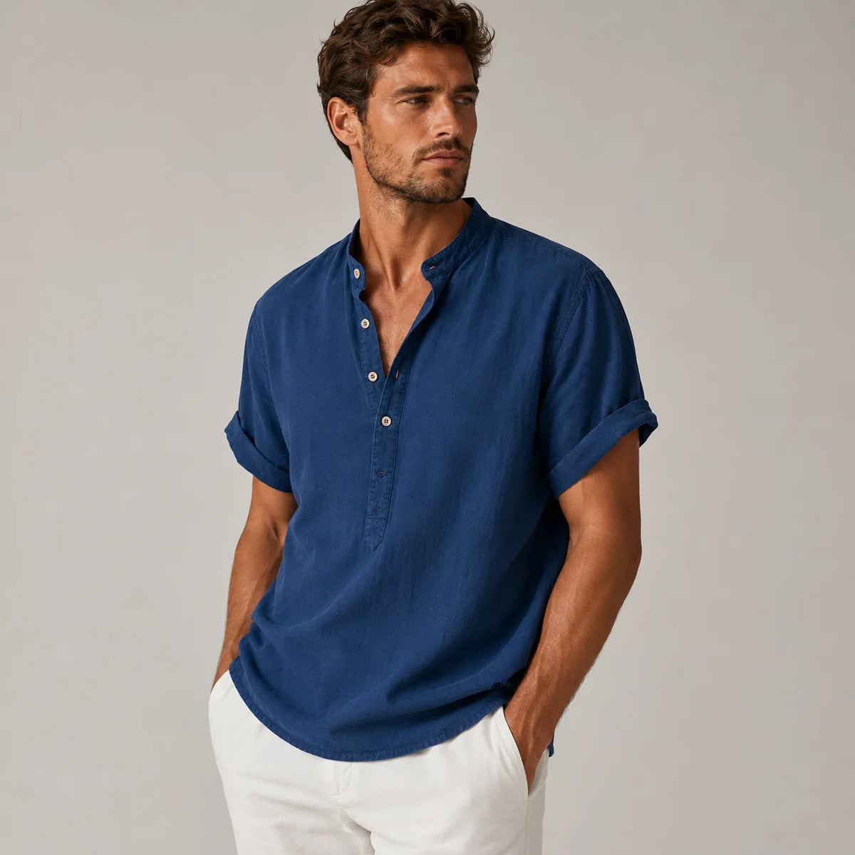Man wearing a navy blue band-collar linen shirt with rolled cuffs, styled with white pants