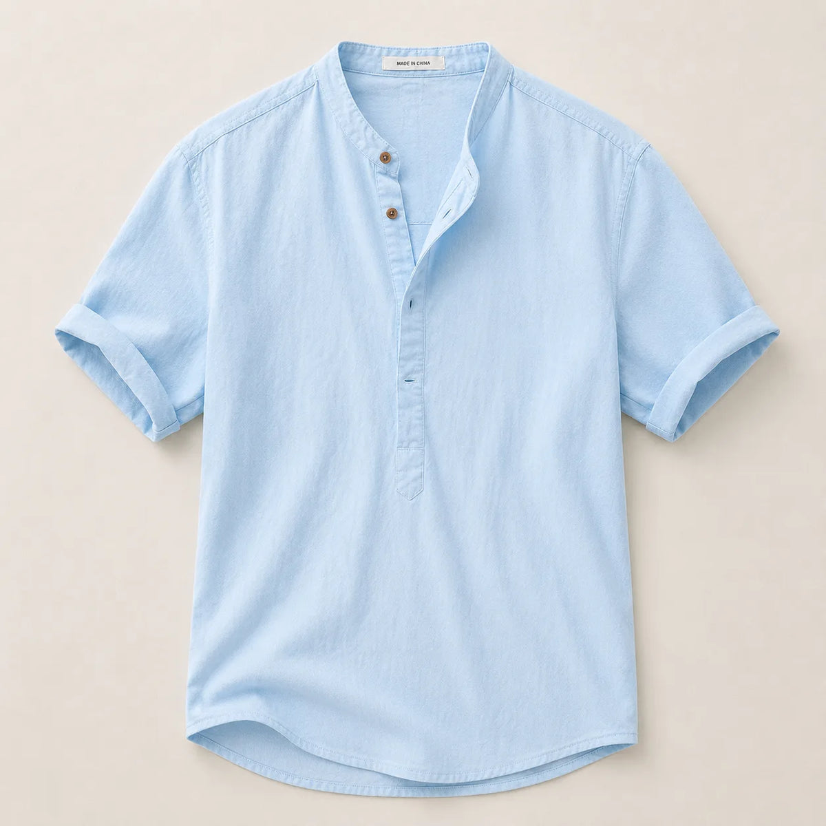 Flat lay of a light blue linen shirt showing the stand collar, button placket and curved hem