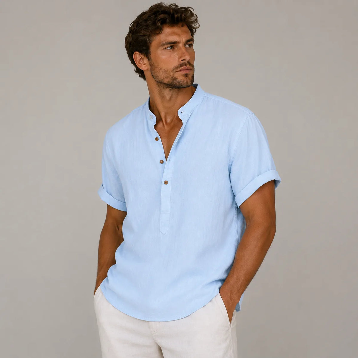 Man in a light blue band-collar linen shirt with sleeves rolled, hands in pockets, worn with cream pants
