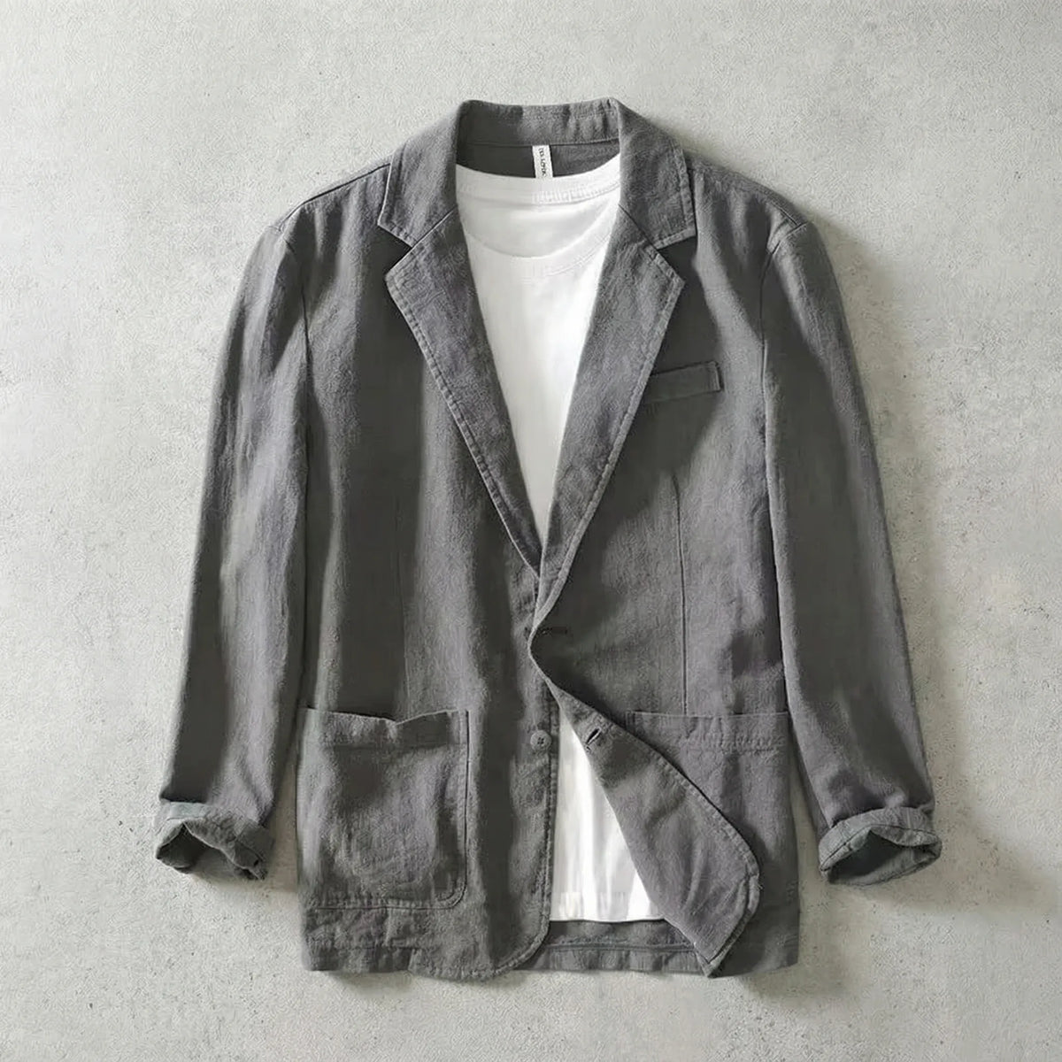 Grey linen-blend blazer worn open over a white t-shirt, showing notch lapels and a chest welt pocket
