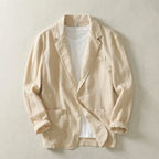 Beige linen blazer laid flat, unbuttoned over a white tee, highlighting the relaxed collar and patch pockets