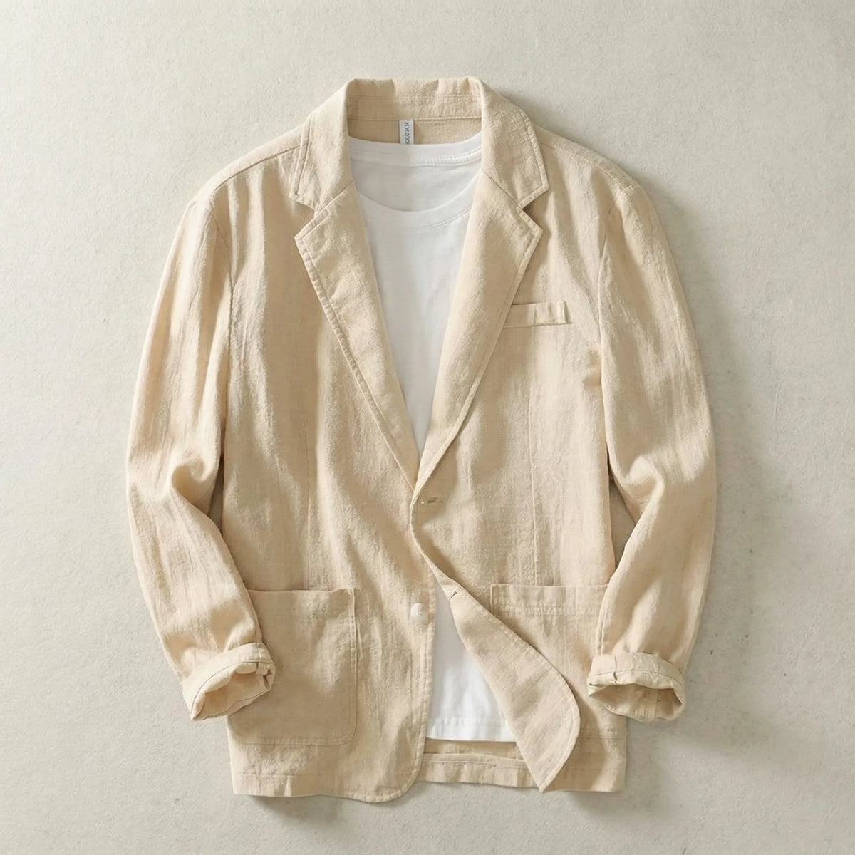 Beige linen blazer laid flat, unbuttoned over a white tee, highlighting the relaxed collar and patch pockets