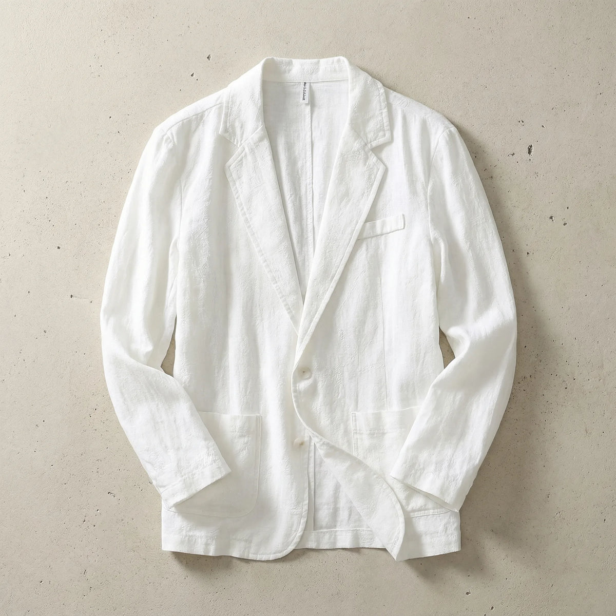 White textured linen blazer laid flat, open front, showing the chest pocket and two-button closure