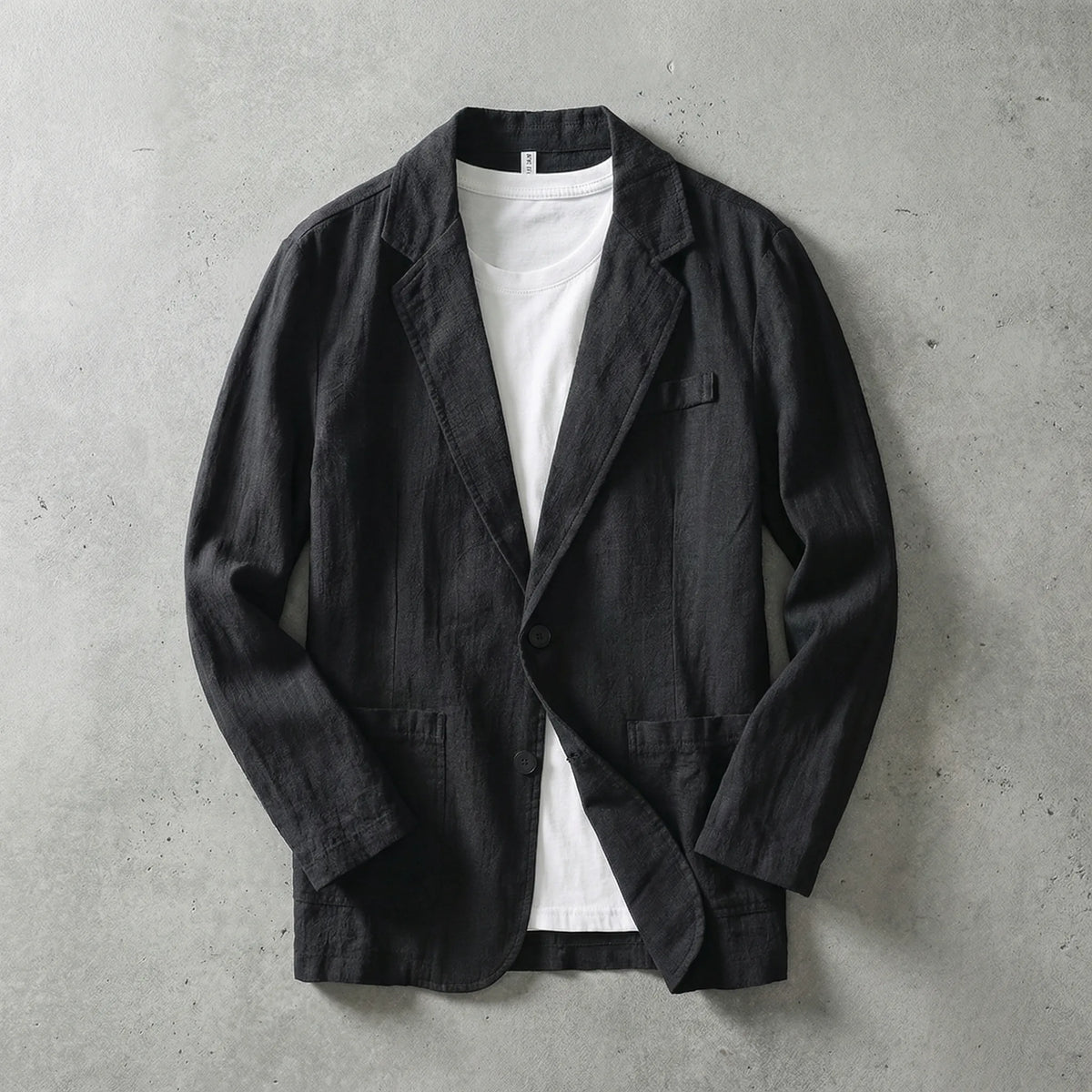 Black linen blazer laid flat and open, showing visible stitching, lapels and twin patch pockets