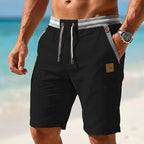 Black linen-blend shorts with grey striped elastic waistband and contrast drawstring, front-on beach shot