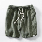 Flat lay of green pinstripe linen-blend shorts with elastic drawstring waist on a grey background