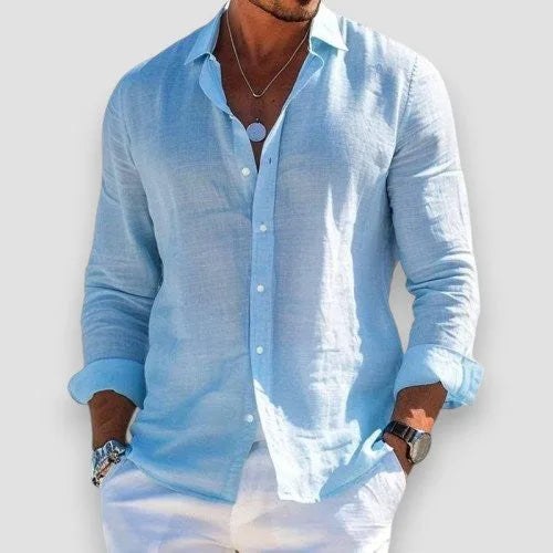 Light blue linen-blend shirt with collar open, sleeves rolled to the forearm, paired with white pants