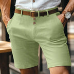 Light green linen shorts with brown leather belt, worn with hands in pockets showing relaxed straight fit
