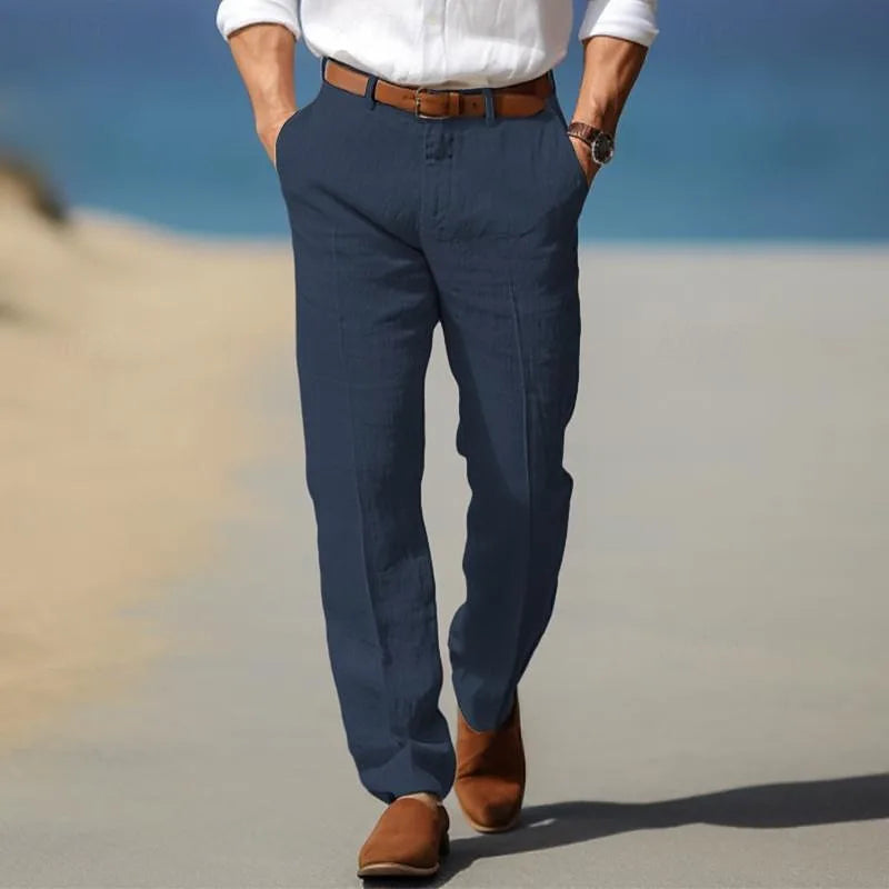 Rear view of man in navy blue linen trousers walking on a sandy coastal path