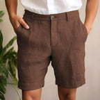 Front view of chocolate brown linen shorts worn with a white linen shirt, hands tucked in pockets