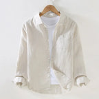 Cream linen shirt on a wooden hanger, front view with buttoned placket, chest pocket and rolled cuffs over a white tee