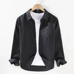 Black linen shirt on a hanger, front view showing buttoned placket, collar and single chest pocket