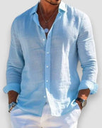 Close view of a man wearing a light blue linen button-up shirt with collar open, paired with white pants