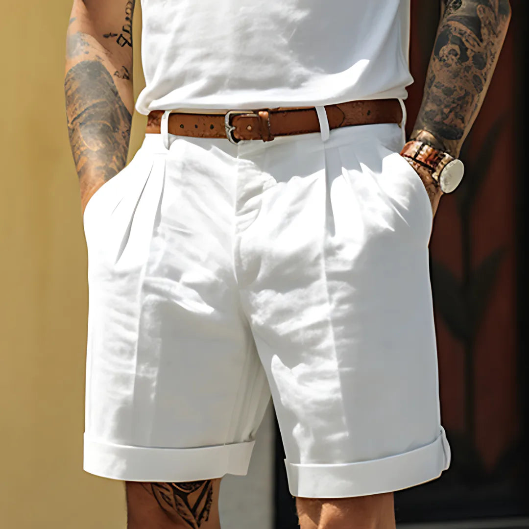Close-up of white tailored linen cotton shorts with belt, pleated front and cuffed hem, worn with a white tee