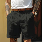 Black tailored shorts with pleated front, belted waist and rolled cuff, styled with a white tee