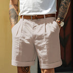 Light grey tailored shorts with pleated front and cuffed hem, paired with a tan leather belt