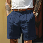 Navy tailored shorts with pleated front, belt loops and folded cuff hem, close-up front view