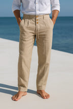 Close-up front view of beige linen pants with wooden buttons, belt loops and drawstring waist tie