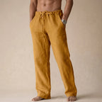 Front view of mustard gold linen trousers with drawstring waist and hands in pockets
