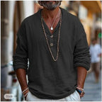 Man in a black linen popover shirt with relaxed V-neck collar, standing outdoors on a cobblestone street.
